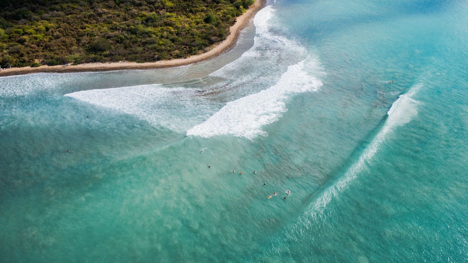 Aerial view of pristine turquoise waves breaking on tropical shoreline.