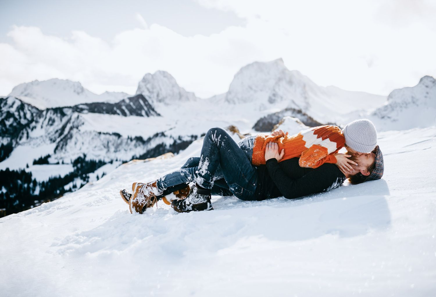 Person lying in snow with mountain peaks visible in background.