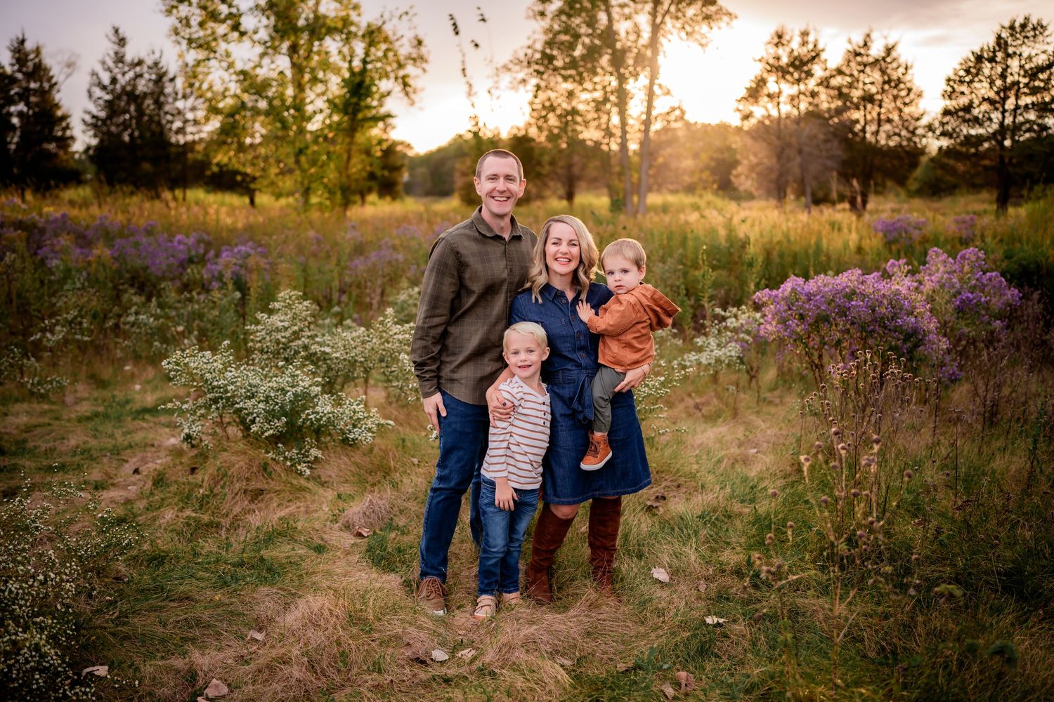 Family portrait in wildflower meadow at golden hour with purple flowers and setting sun.