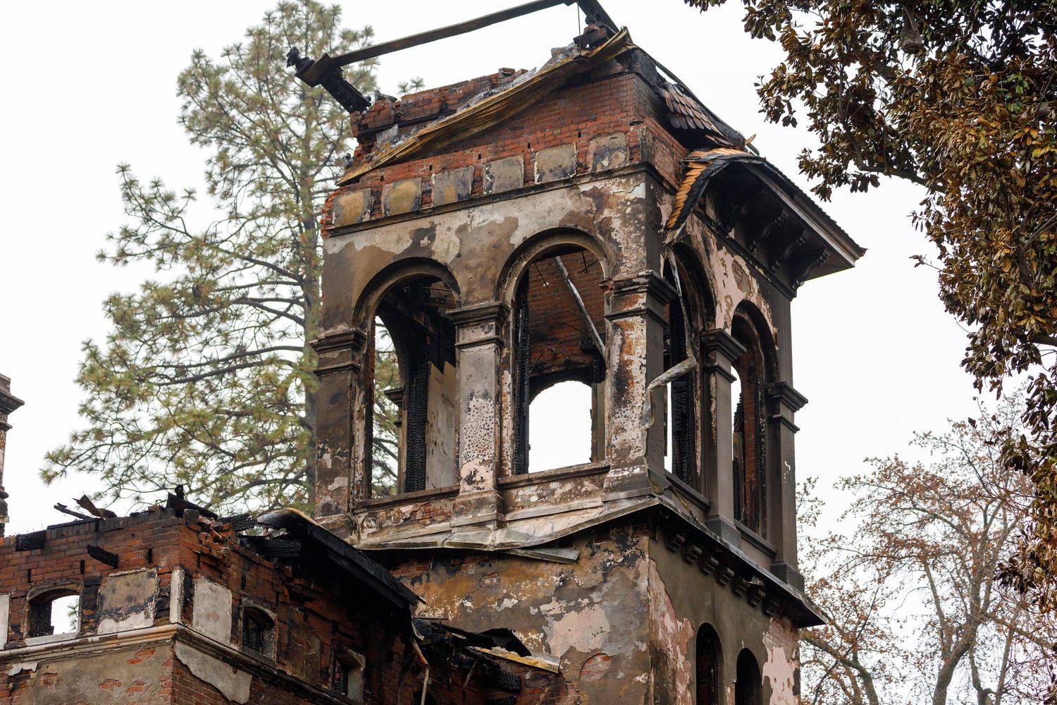 Weathered brick bell tower with arched windows stands deteriorating against autumn trees in historic architecture ruins.