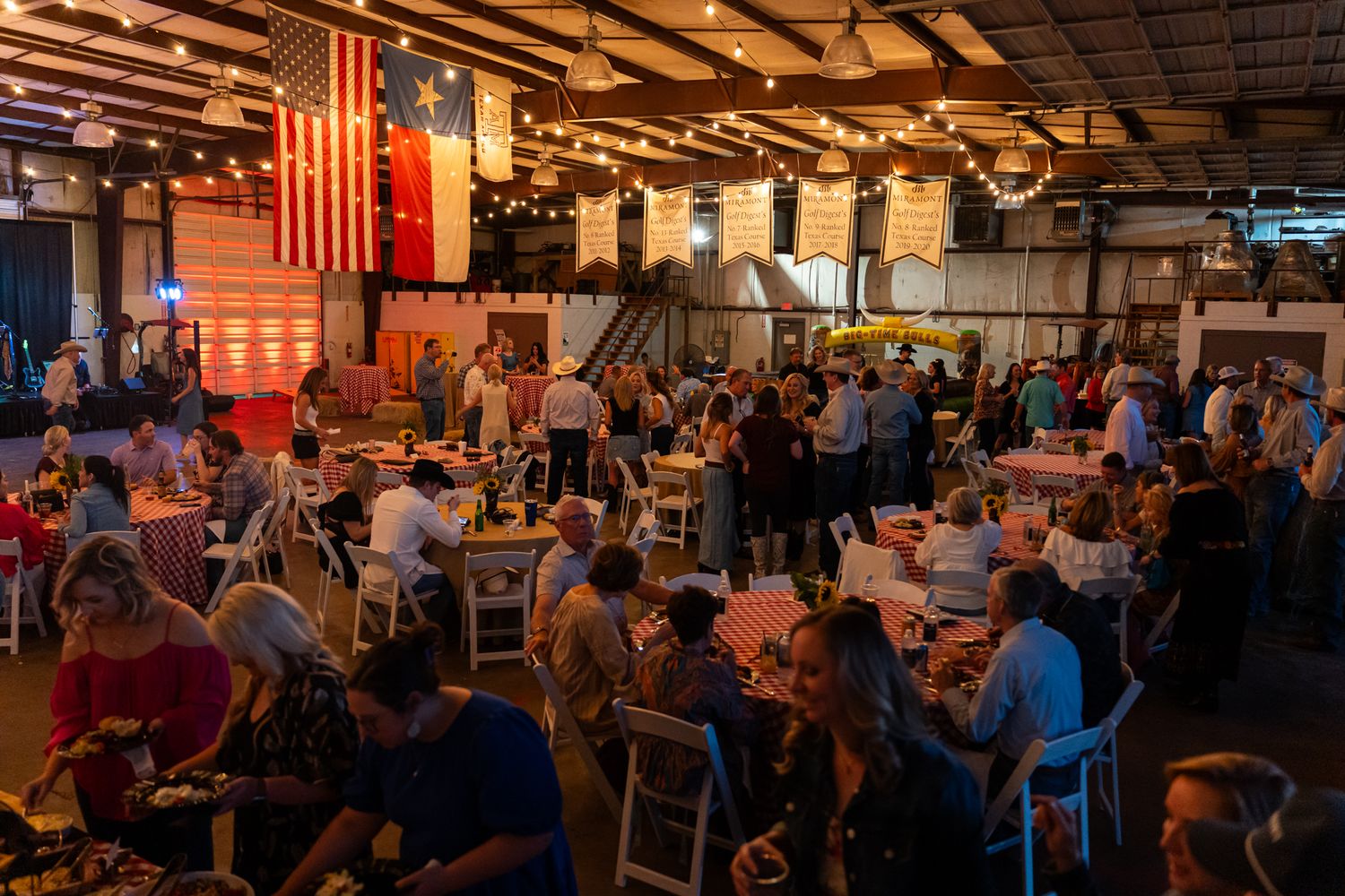 Crowded restaurant interior with American flag and exposed wooden beams illuminated in warm lighting.