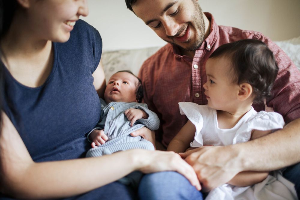 Everett lifestyle newborn photographer: A family of 4 sit on the bed during their newborn photo shoot at home in Everett WA