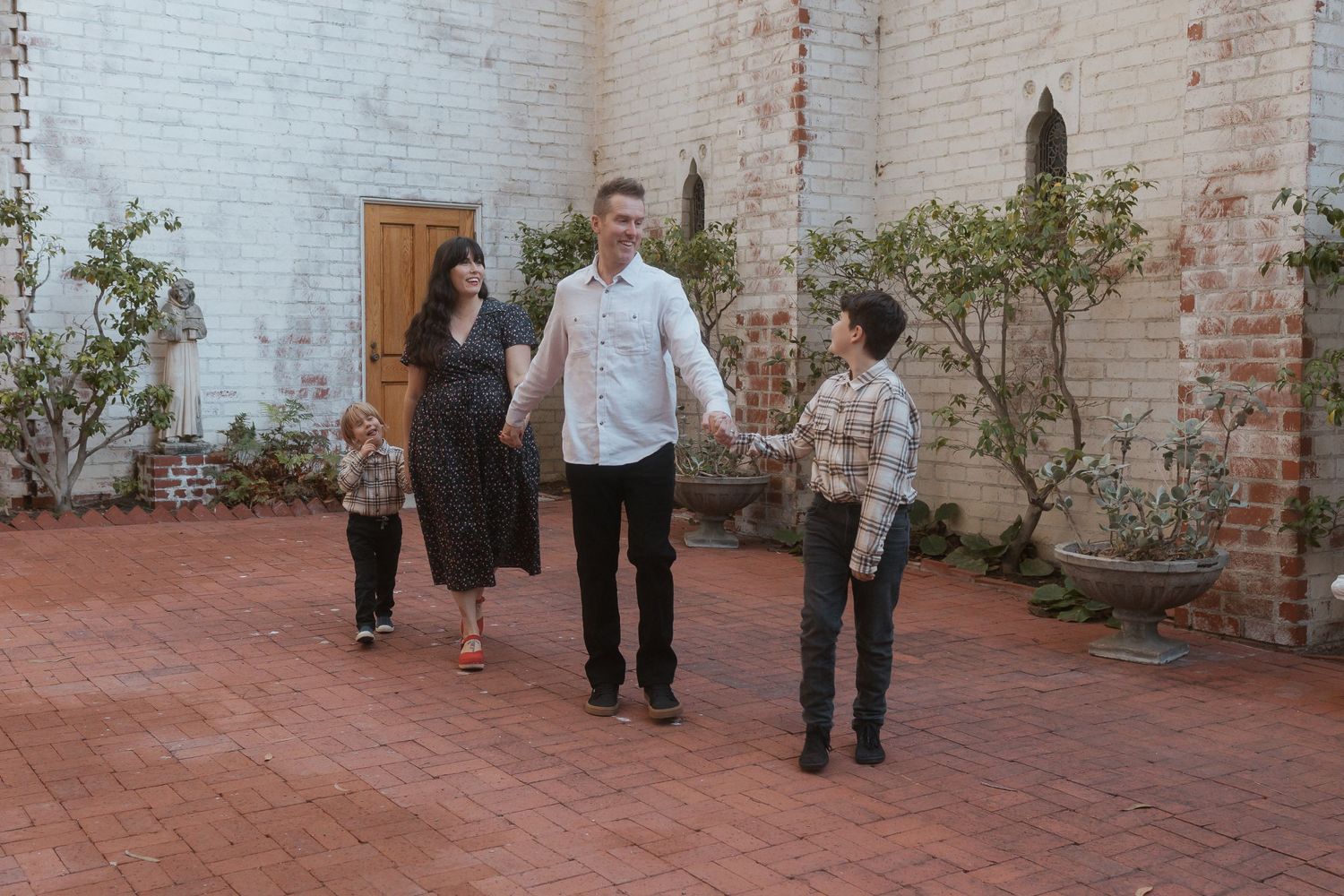 Family walking together on brick patio by white wall with plants.