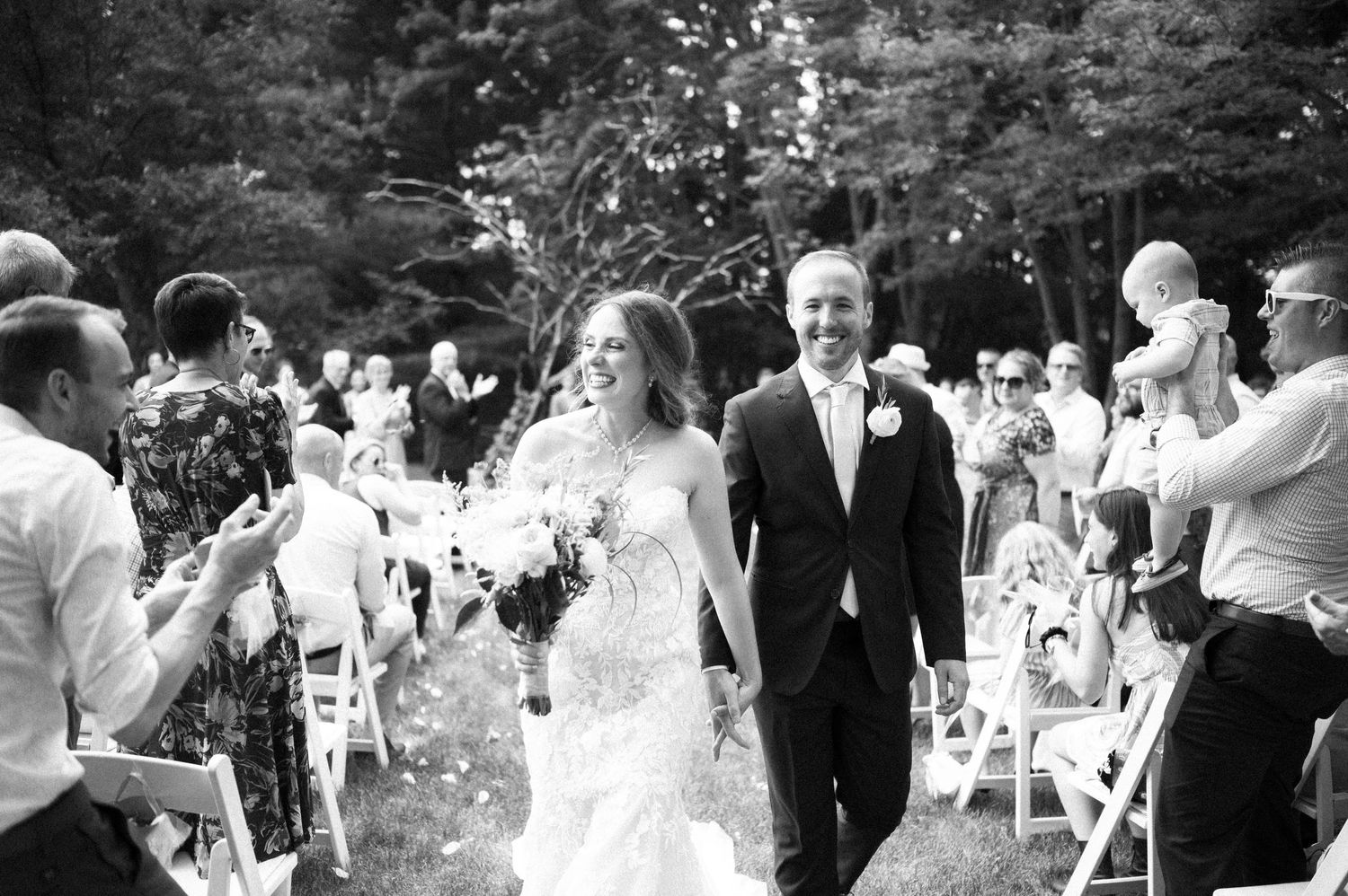 A happy couple exits their outdoor garden wedding ceremony while guests throw flower petals in celebration.