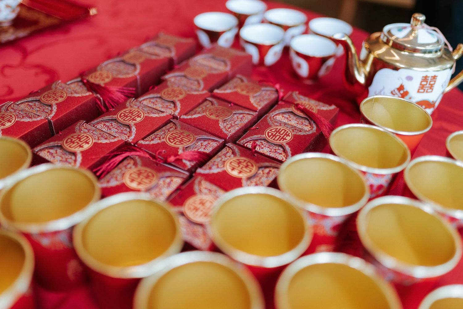 Traditional tea service with red and gold decorative boxes and teacups arranged on red tablecloth.