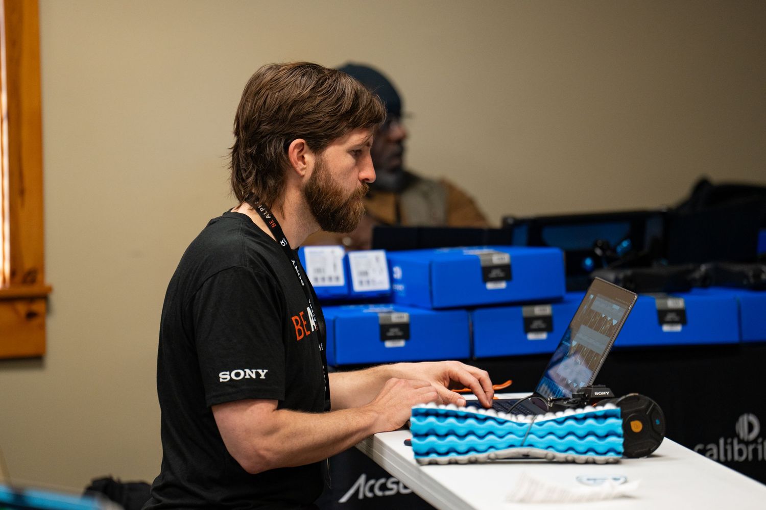 Alex Kent, pro photographer sits at this laptop with his Sony shirt and gear beside him.