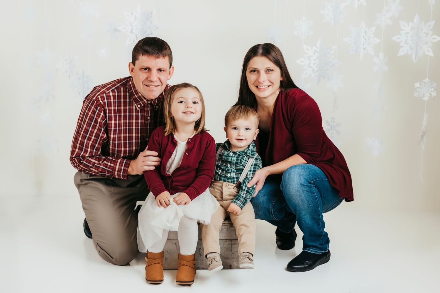 Holiday portrait of a family of four against a snowy backdrop with white snowflakes.