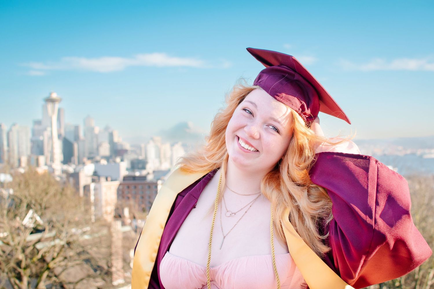 Senior girl in maroon gown posing at Kerry Park with Seattle skyline in background