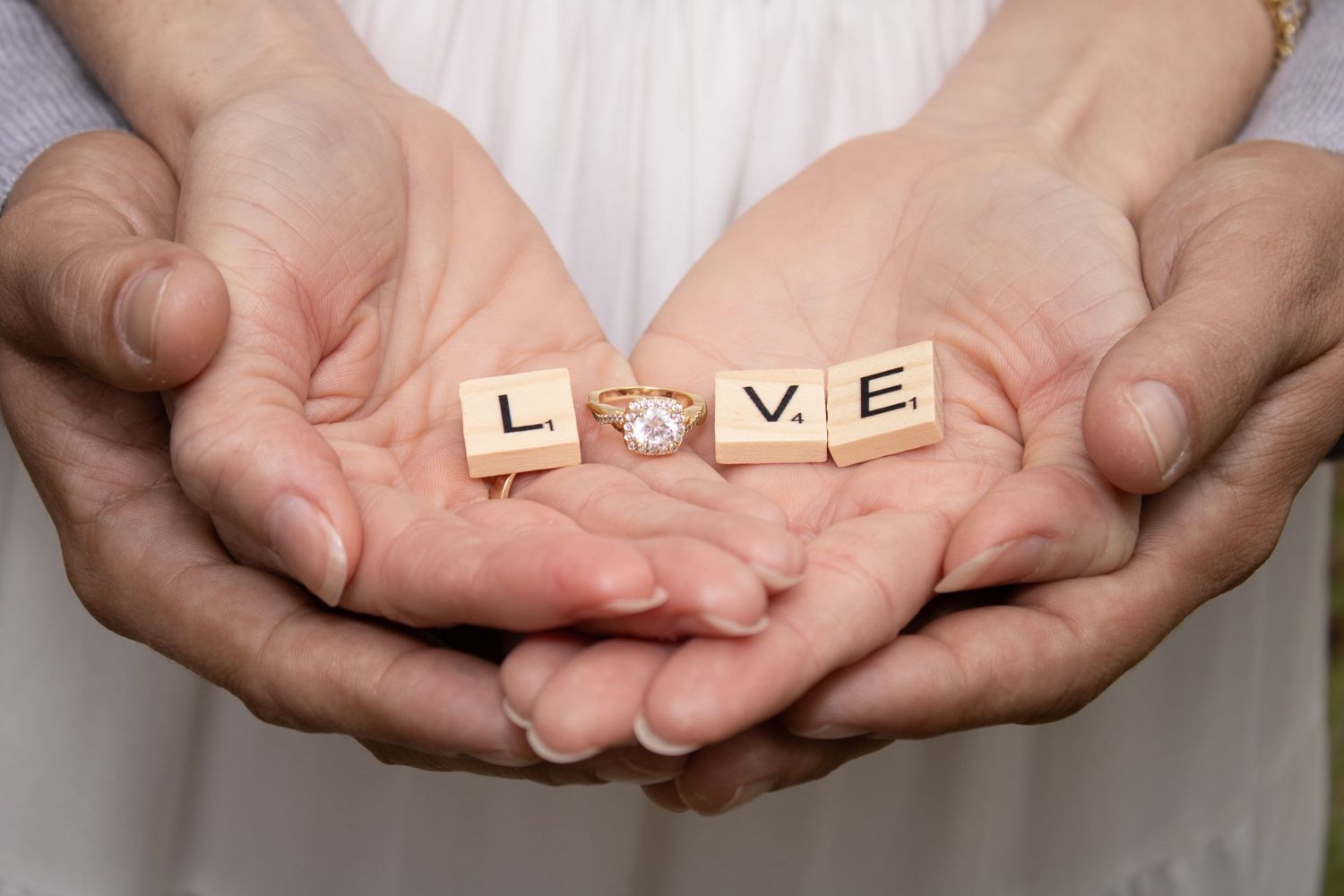 Hands holding wooden letter tiles spelling out LOVE with a diamond ring.