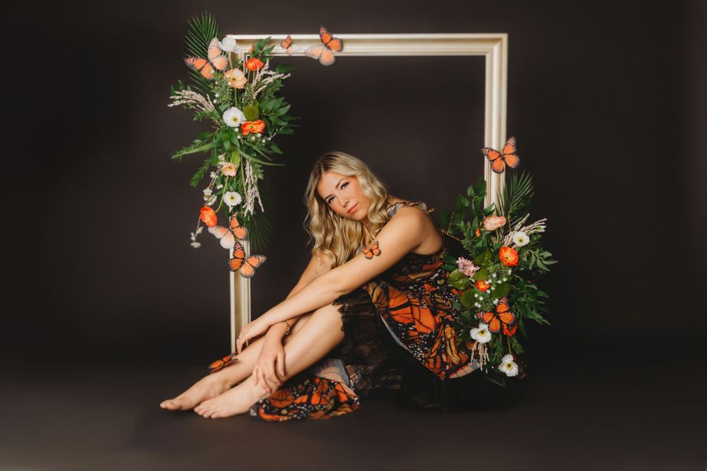 Dramatic studio portrait with decorative frame and floral elements against black backdrop.