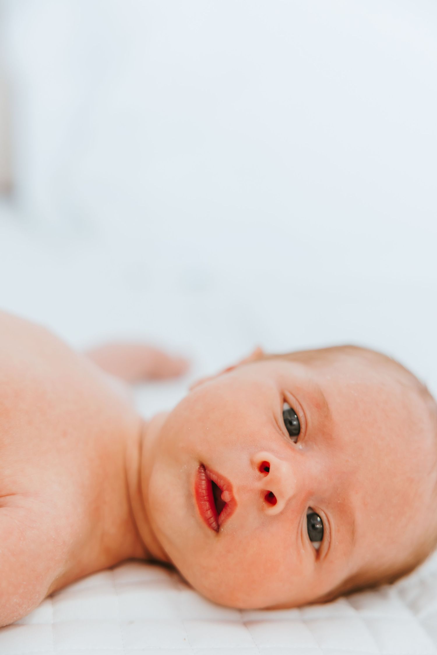 Closeup view of a baby lying sideways on white bedding looking at the camera.