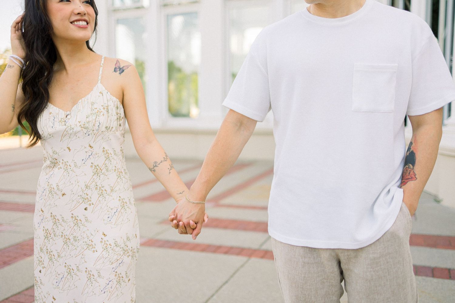 Couple holding hands walking in casual summer outfits on paved walkway.
