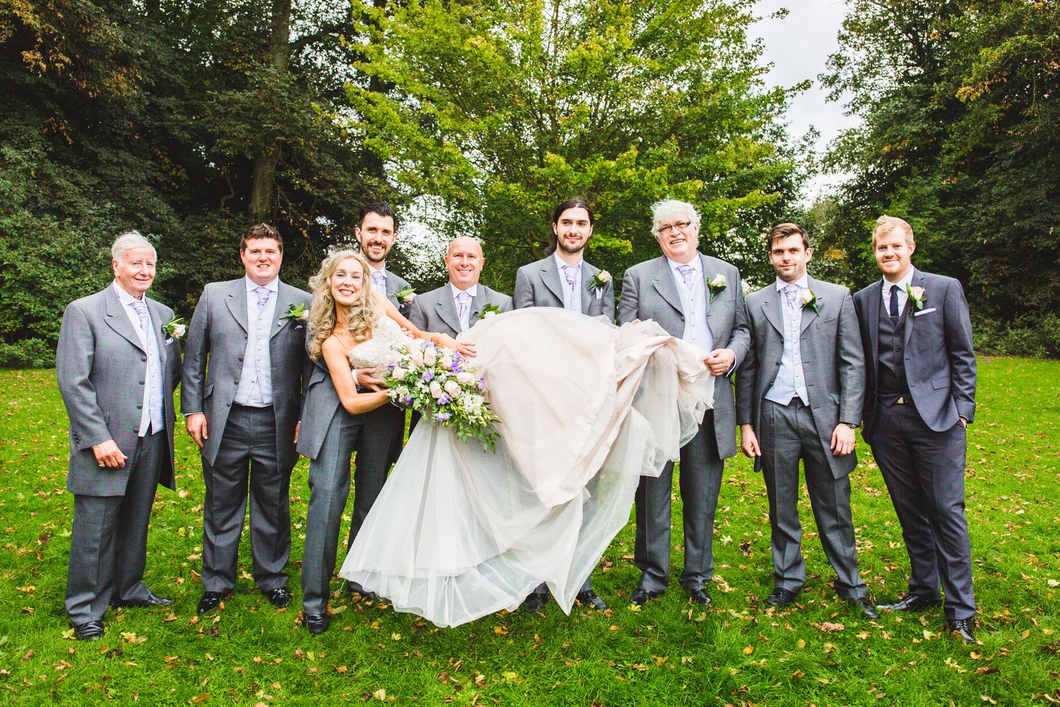 Wedding party posing for a group photo in a lush green garden setting.