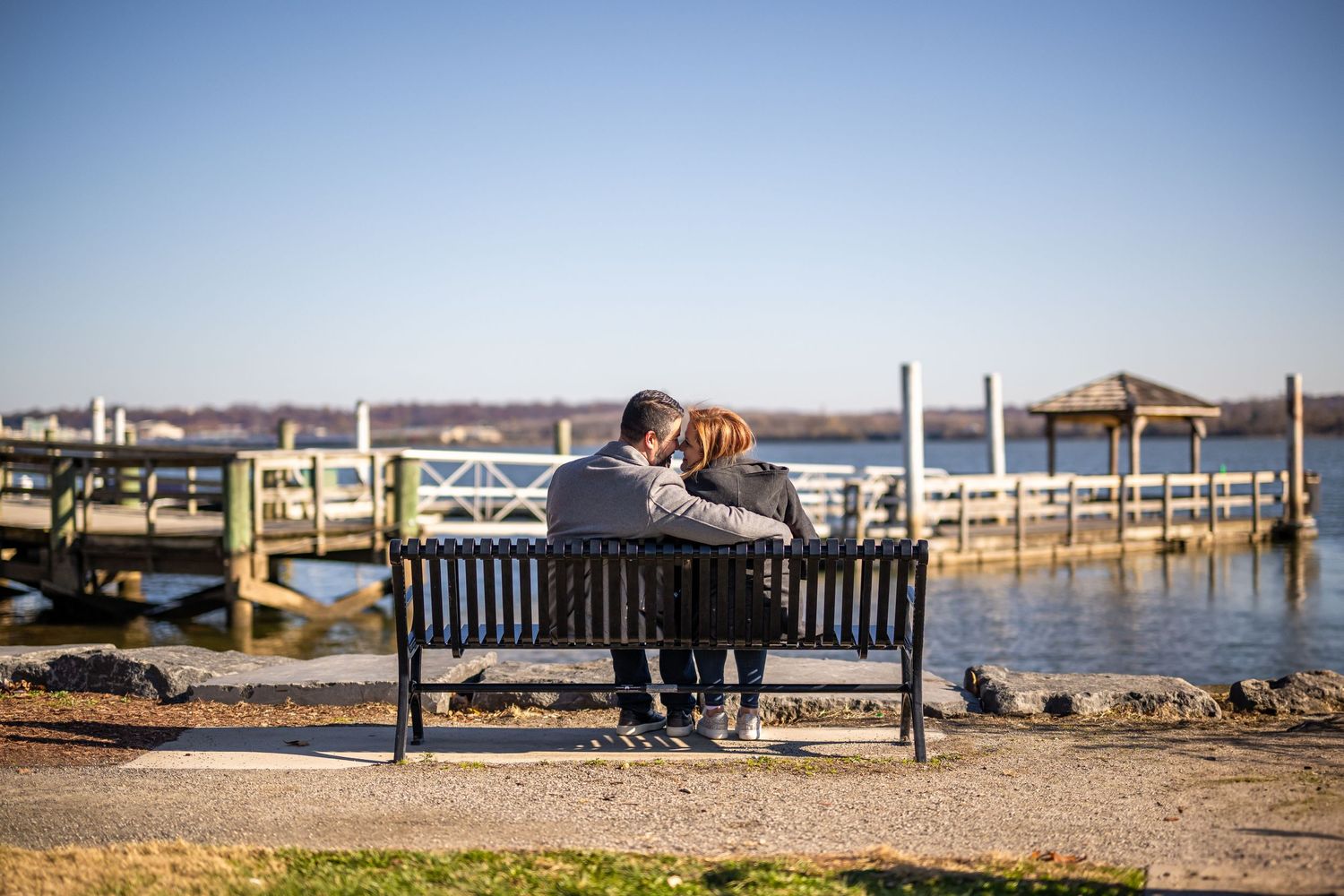 Couple sharing a tender moment on a bench overlooking a marina with boats and docks.
