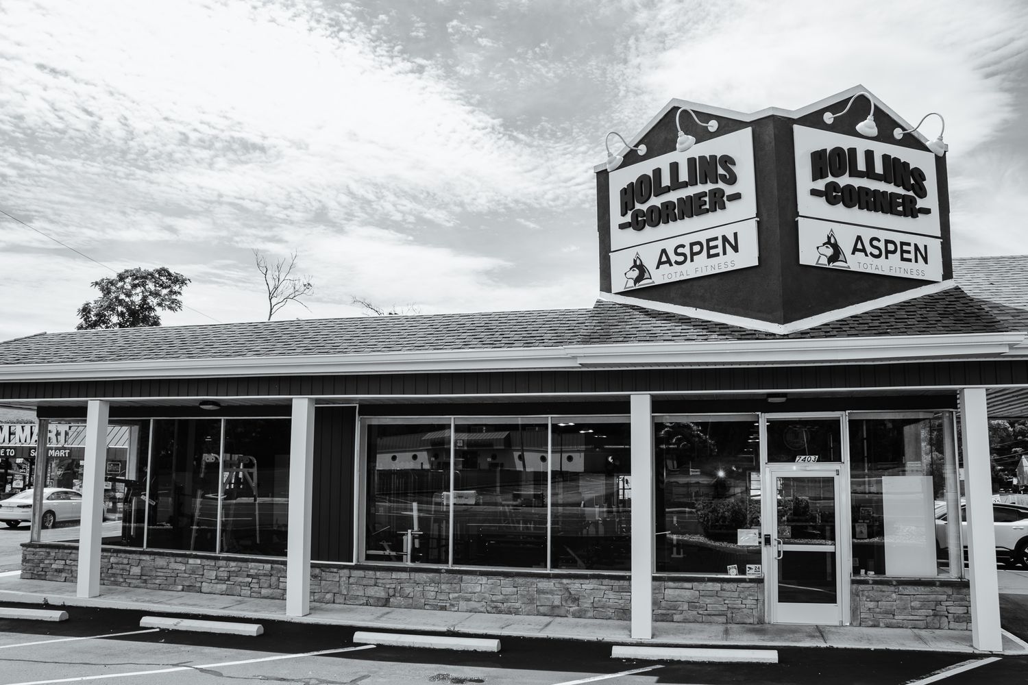Black & white photo of Aspen Total Fitness at Hollins Corner with large front windows and a rooftop sign above the entrance