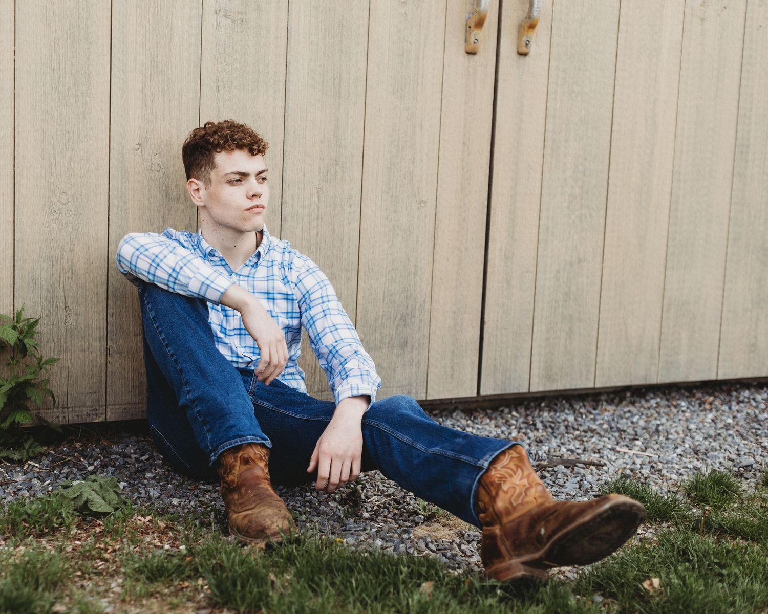 Professional senior photo of a young man sitting by a barn