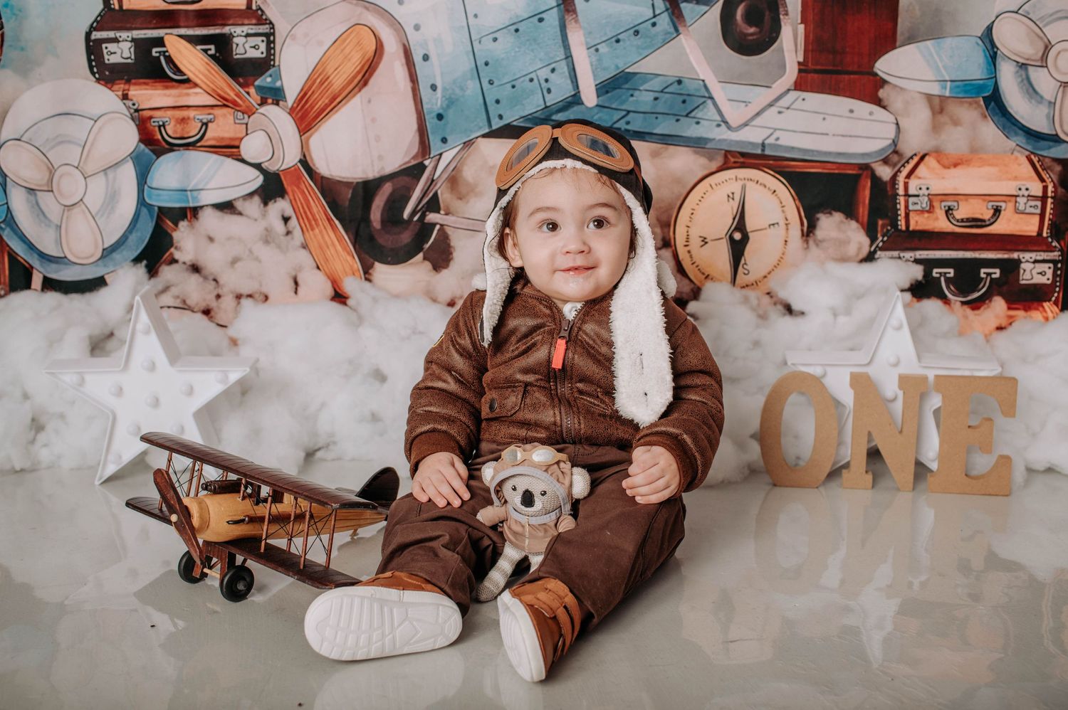 A vintage aviation themed photo of a baby wearing a brown outfit with toy planes and clocks.