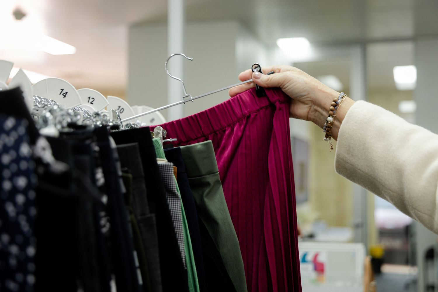 Two elderly women having an animated conversation while shopping in a retail store with clothing racks visible.