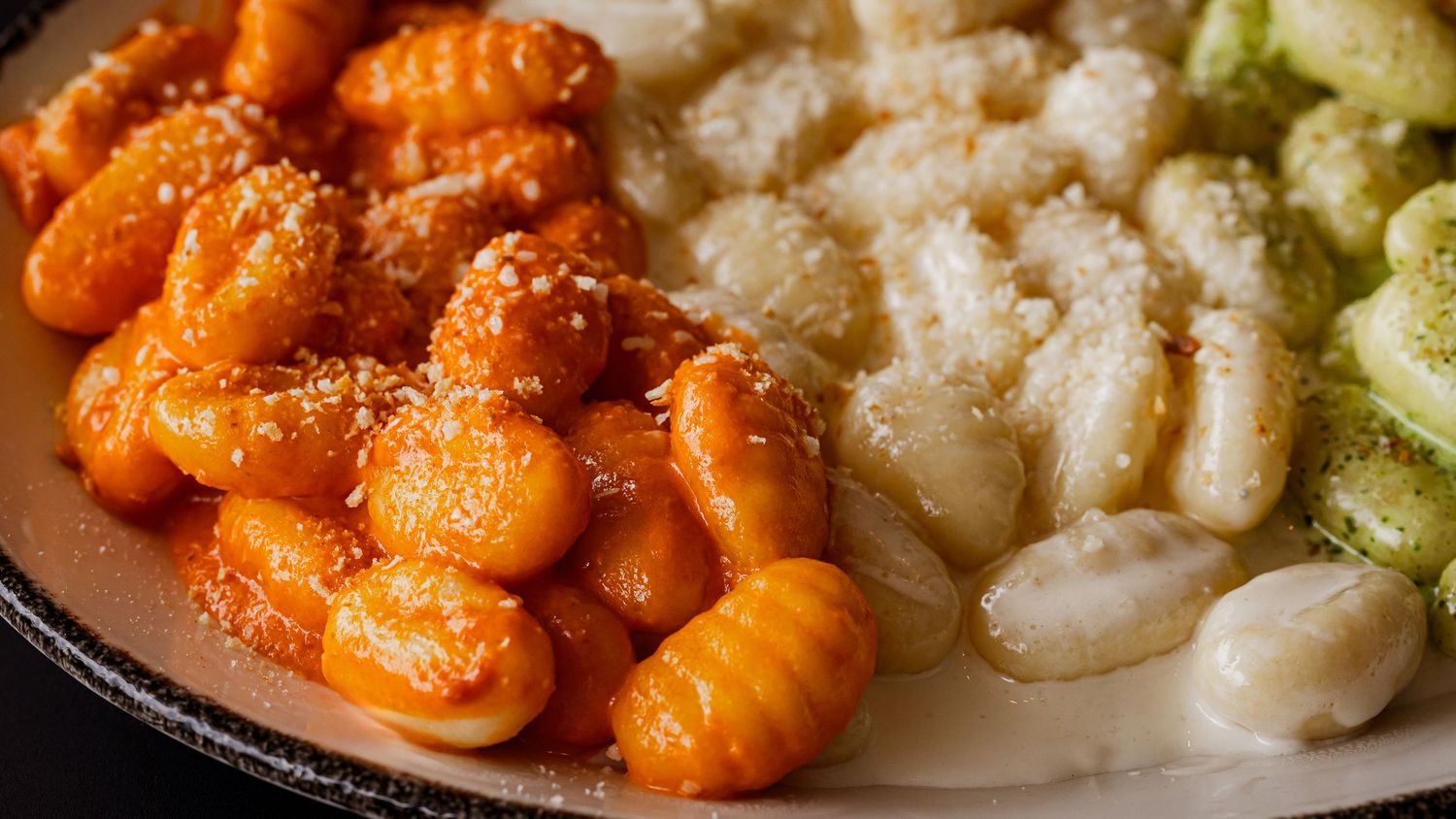 A plate of tri-colored gnocchi featuring saucy orange, plain white, and green varieties topped with sesame seeds.