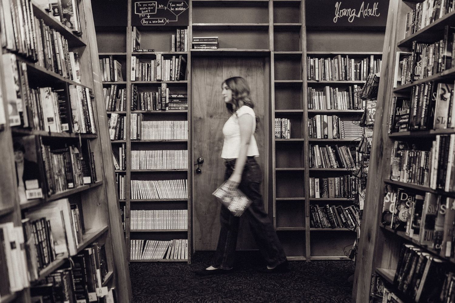 Woman browsing shelves in a cozy bookstore aisle, black and white photo capturing a love of reading.