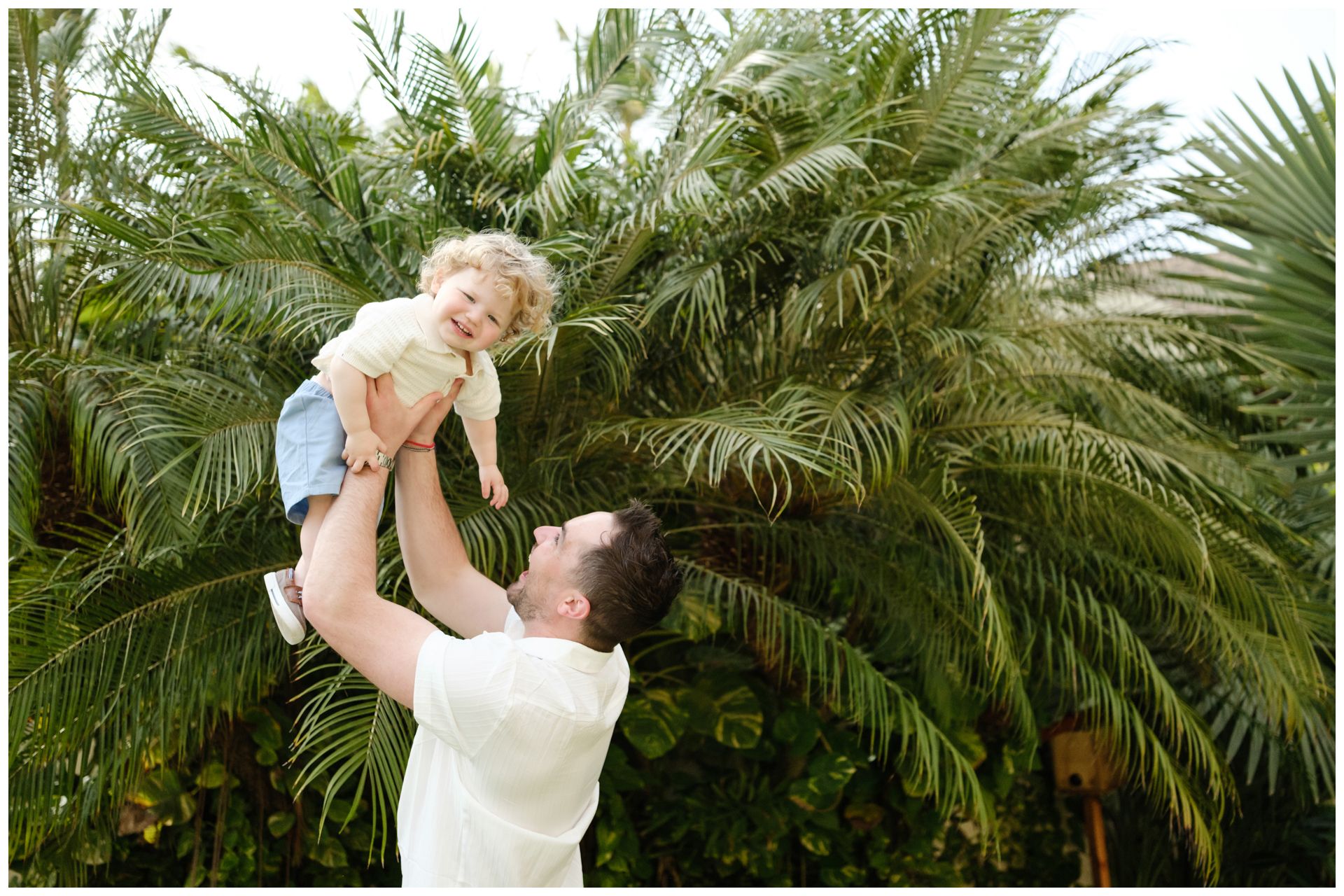 A family plays together on a beach, lifting a child in the air while wearing white clothing in black and white photography.