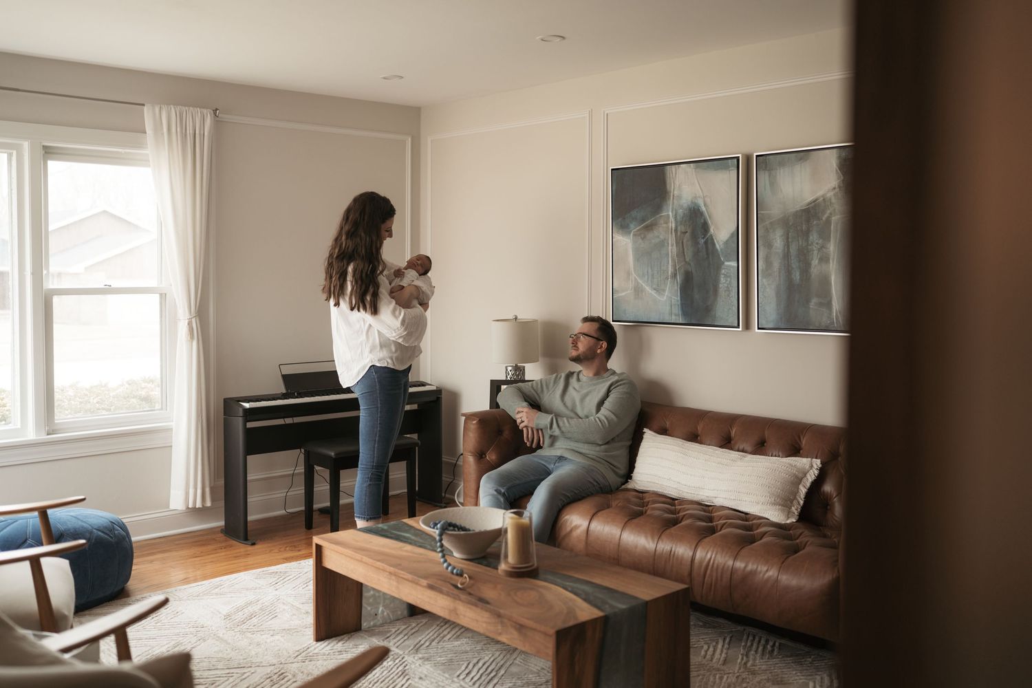Family relaxing in a cozy living room with leather sofa, piano, and natural light from large windows.