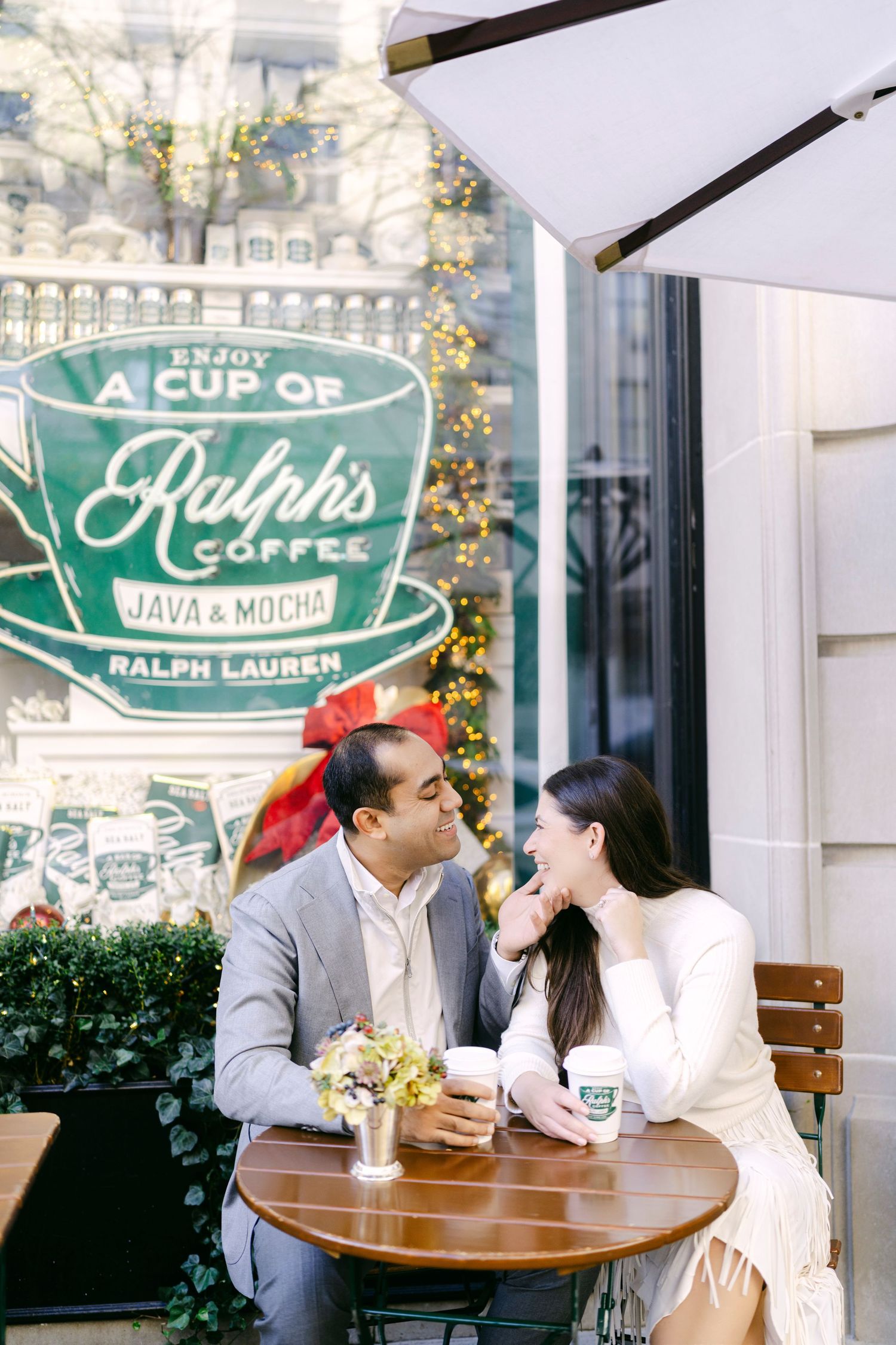 A couple shares a romantic moment at an outdoor cafe with green signage and string lights in the background.