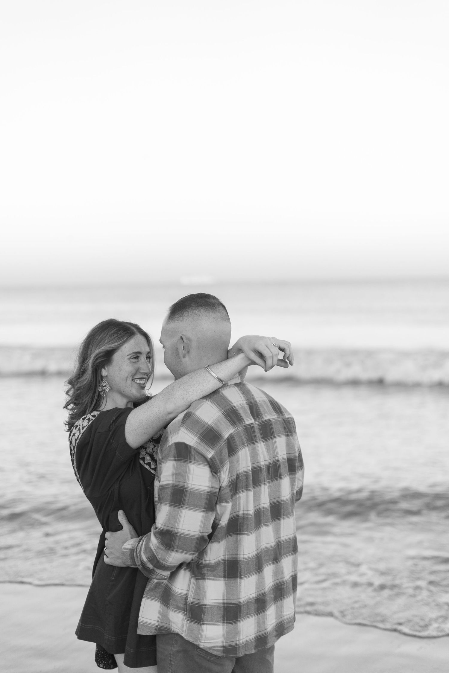 A couple embraces on a beach in black and white, with multiple sequential shots showing their tender moment.