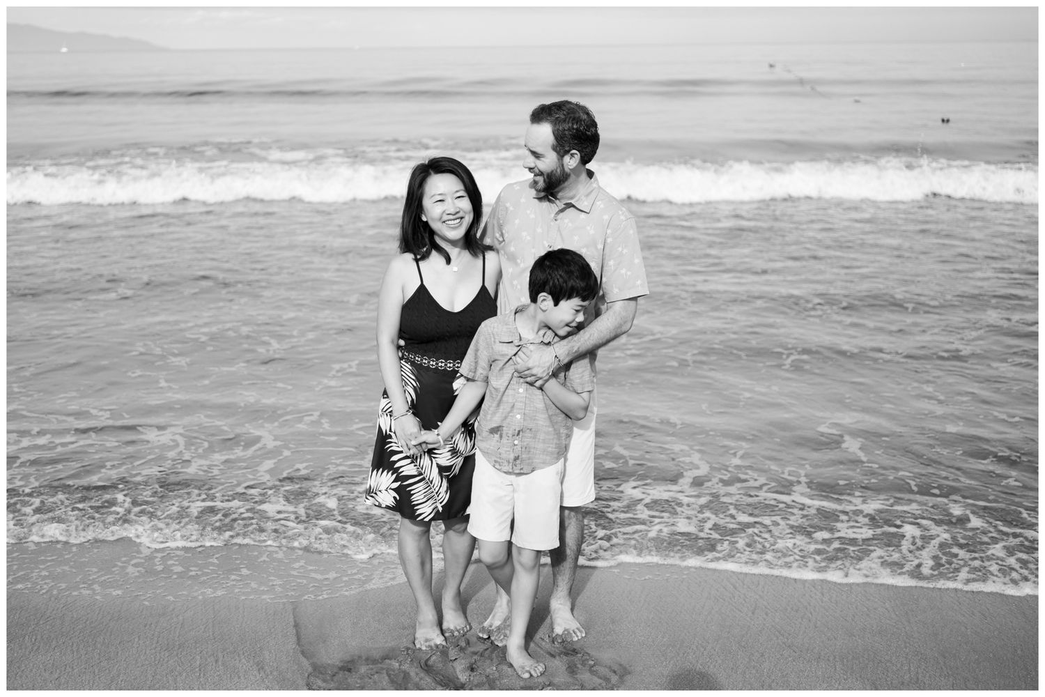 Parents lifting their child while playing on the beach during a family session at Grand Velas Riviera Nayarit, captured in black and white.