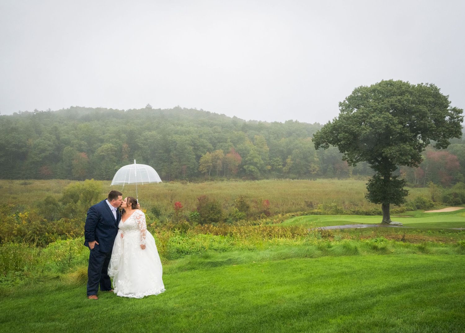 A winter wedding portrait outside a white farmhouse with illuminated windows and a full moon.