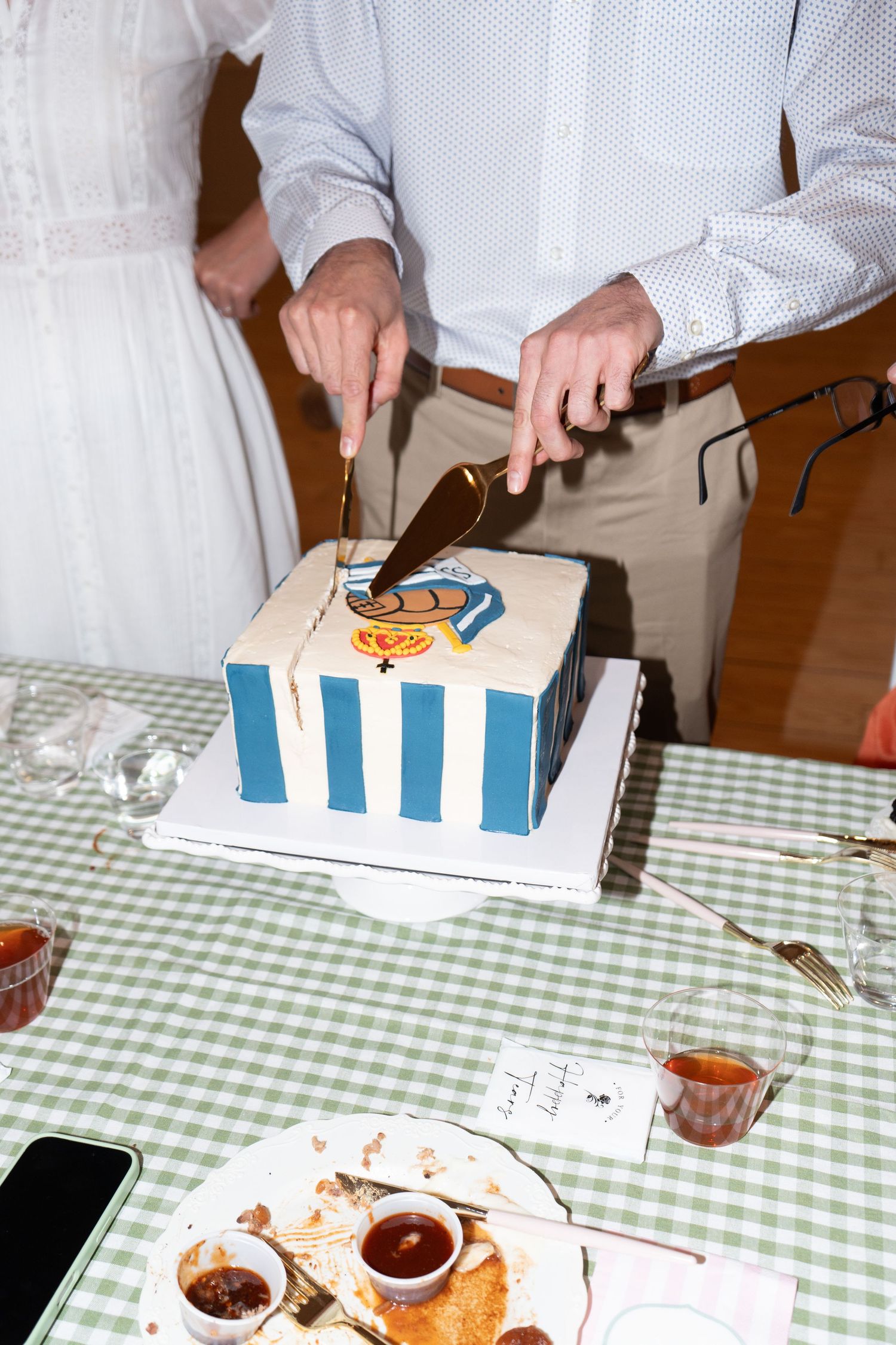 Couple cutting a square blue and white striped wedding cake with Donald Duck design at a reception dinner table.