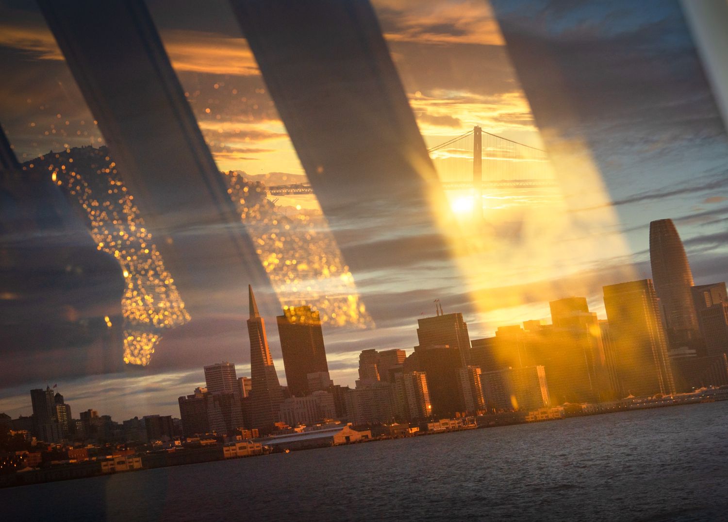 Dramatic sunset over Chicago skyline viewed through bridge beams with golden light streaming through clouds.