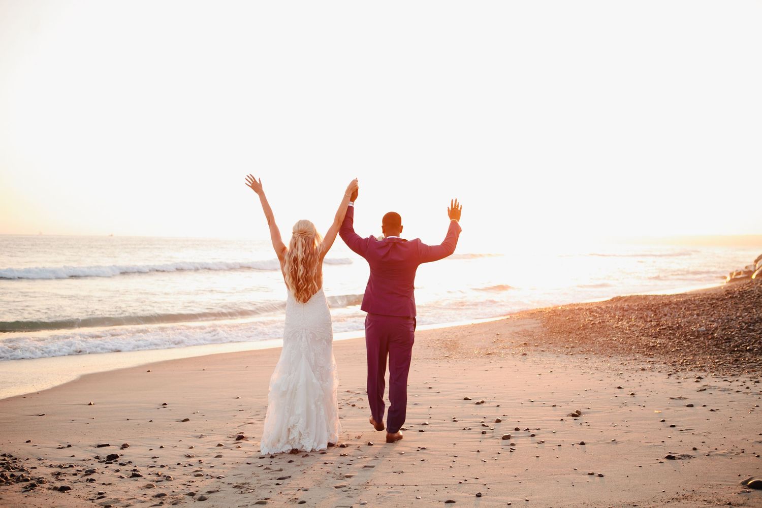 Happy couple celebrates on sandy beach at sunset with arms raised.