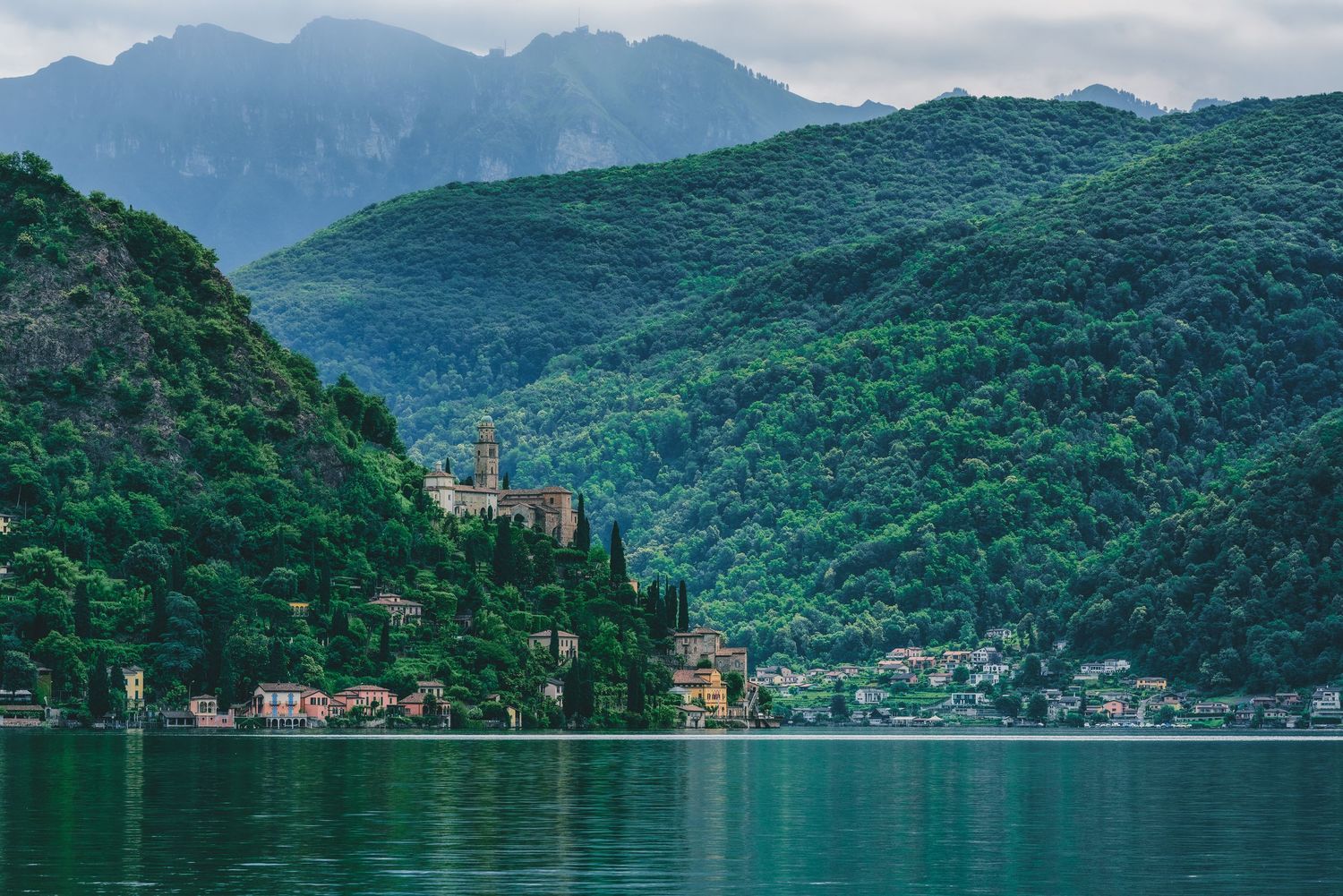 Panoramic view of Lake Como in Italy showcasing forested mountains, waterfront villas and Mediterranean architecture.