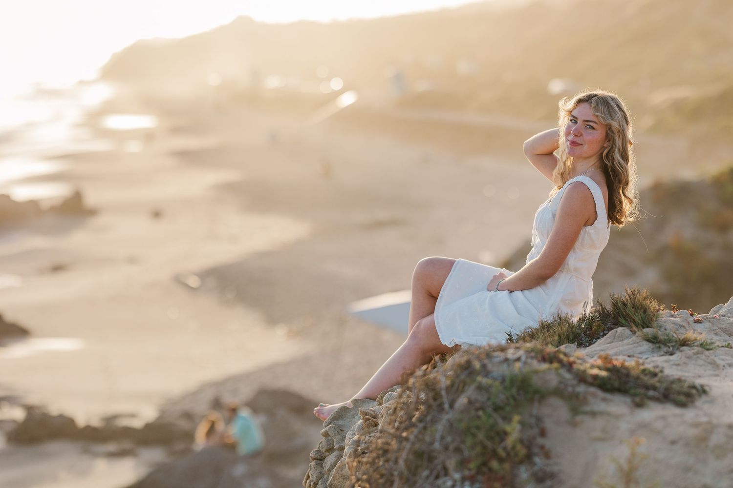 Woman in white tank top and denim shorts poses outdoors during golden hour photoshoot.