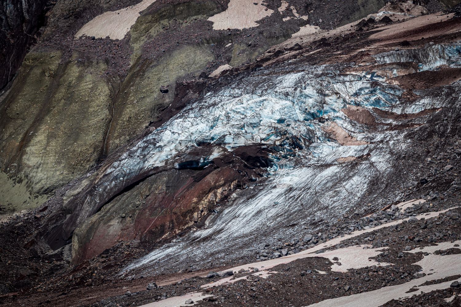 Panoramic aerial view of a snow-covered mountain pass with winding roads and rugged terrain under cloudy skies. Mount Tahoma, Washington