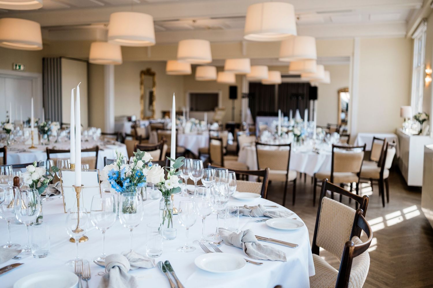Elegant wedding reception venue with round tables, white linens, and pendant lighting creating a sophisticated atmosphere.