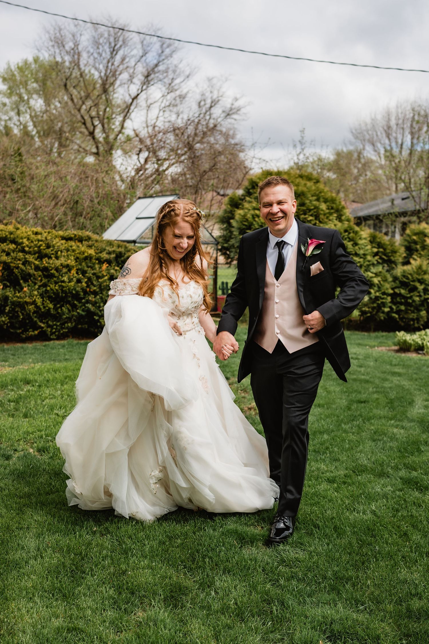 Cynthia + John run towards the camera in their backyard dressed in their wedding outfits.