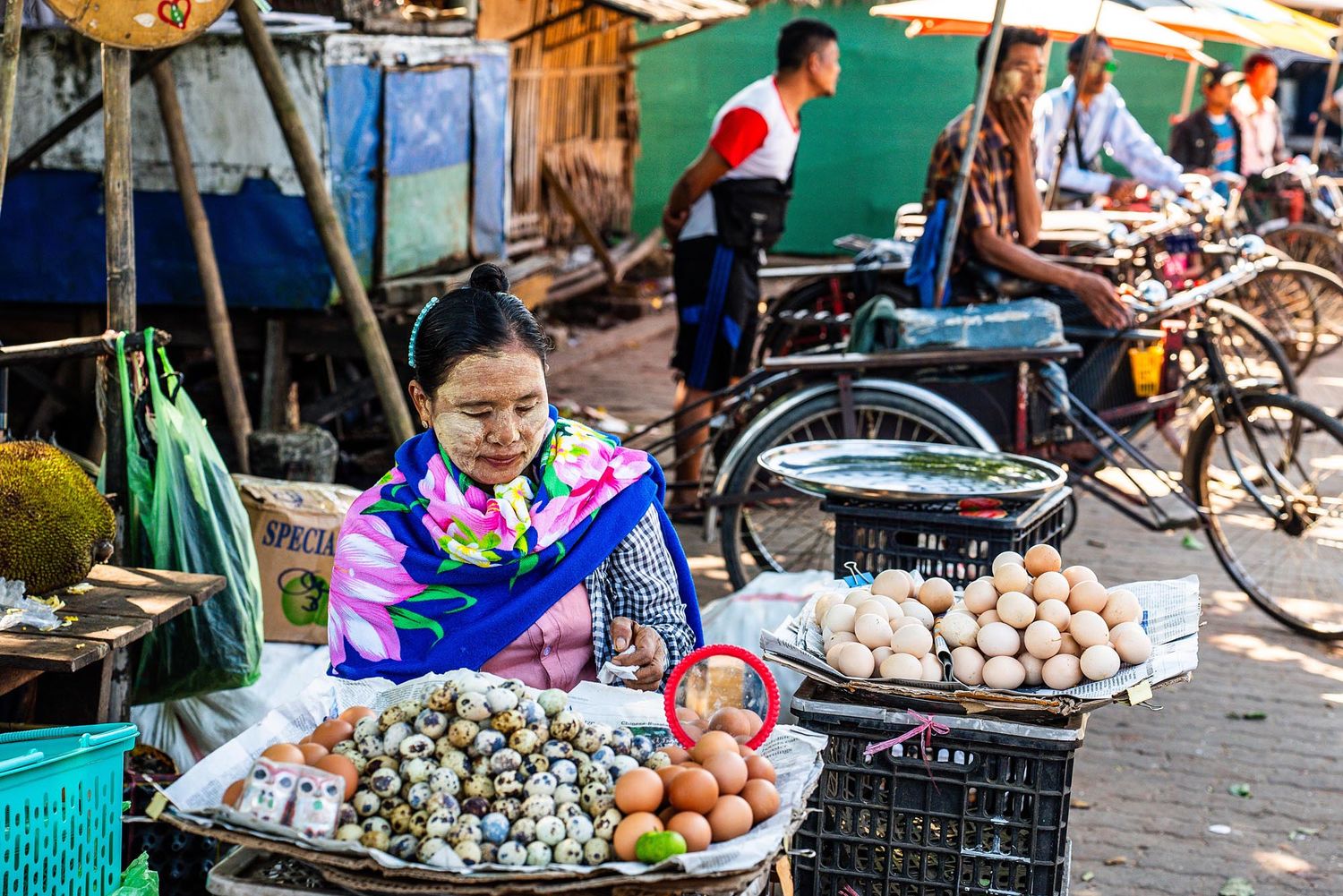 Colorful street market stalls in Asia displaying fresh produce, eggs, and local goods for sale.