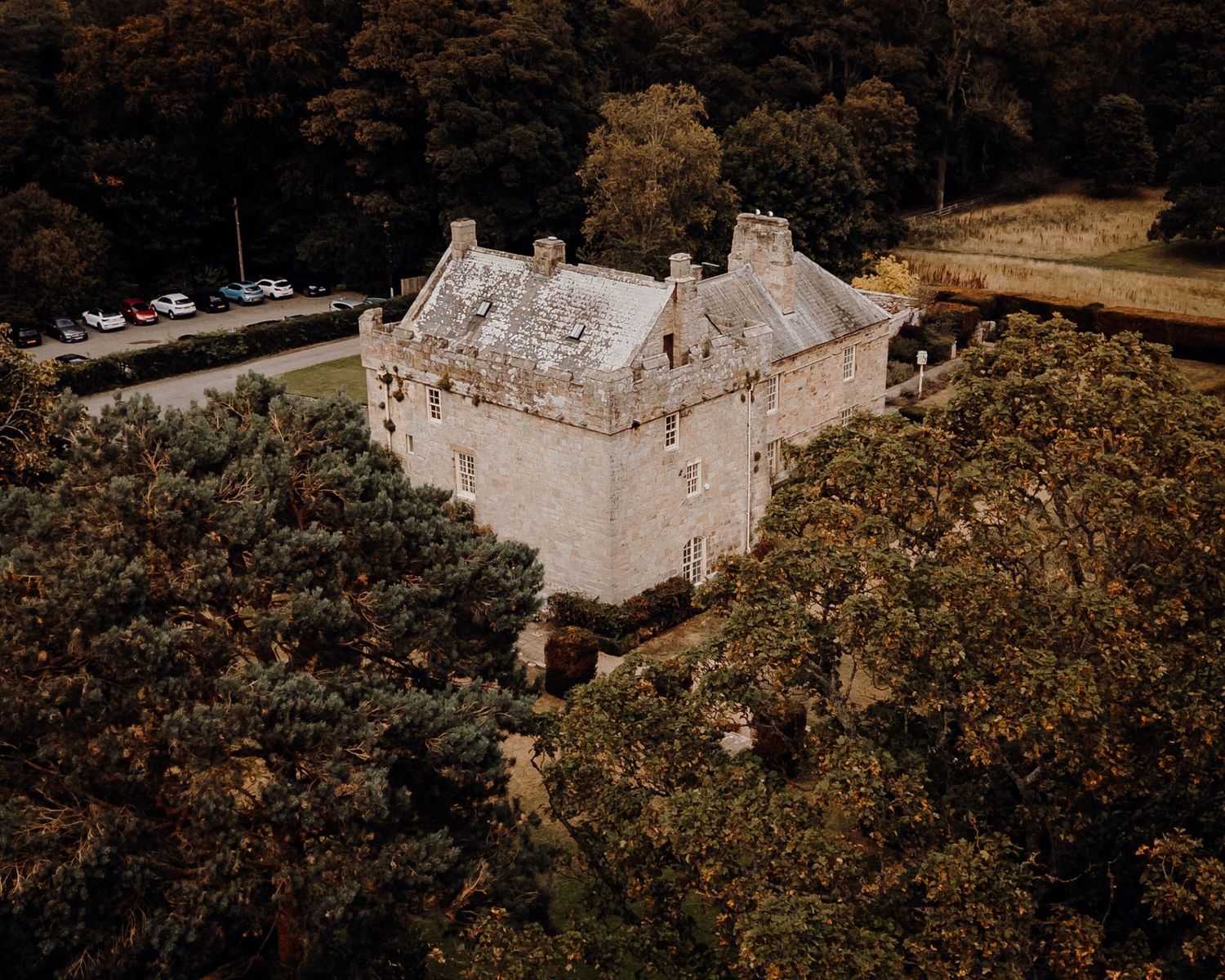 Aerial view of a historic stone castle surrounded by autumn trees and forest in a rural countryside setting.
