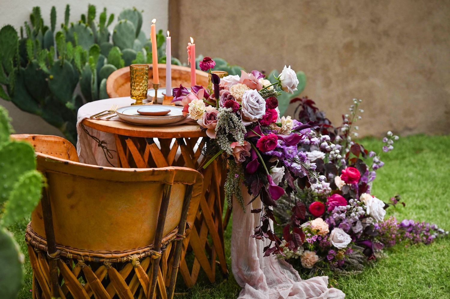 An initiate wooden sweetheart table for a wedding with lush, colorful, cascading flowers set in a garden.