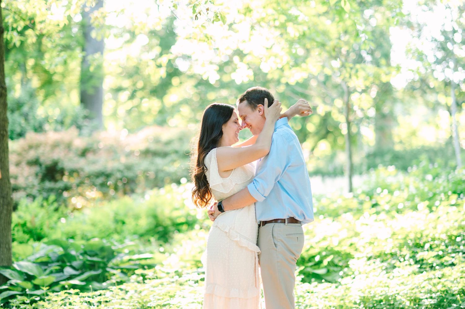 A romantic couple embraces in a sunlit garden setting surrounded by lush greenery.