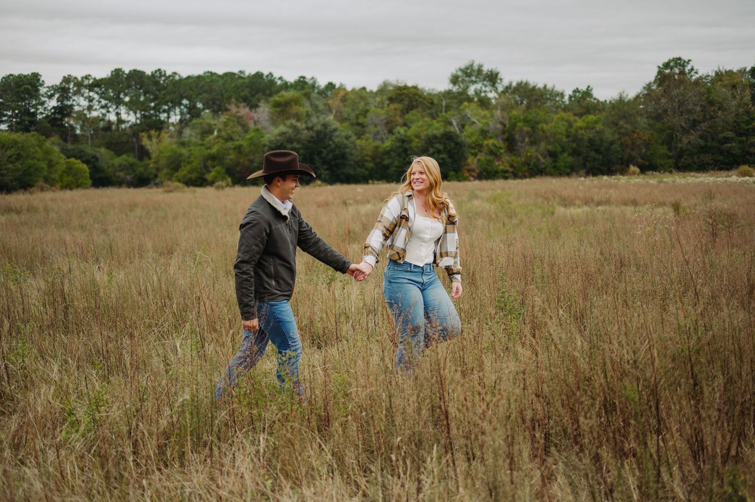 Two people walk together through a tall grass field on an autumn day.