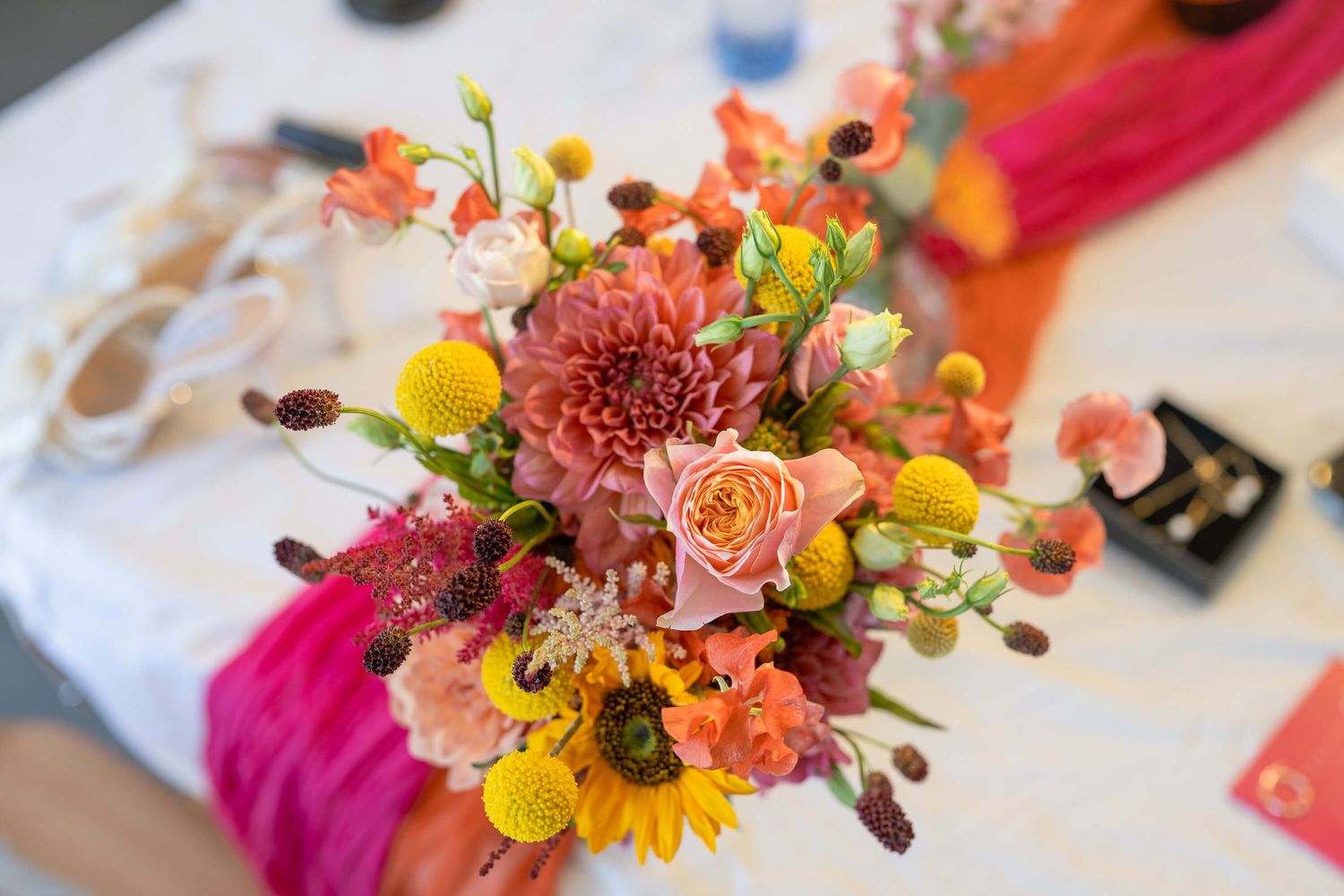 A vibrant floral arrangement features peach, pink, and yellow blooms with eucalyptus accents against a white surface.