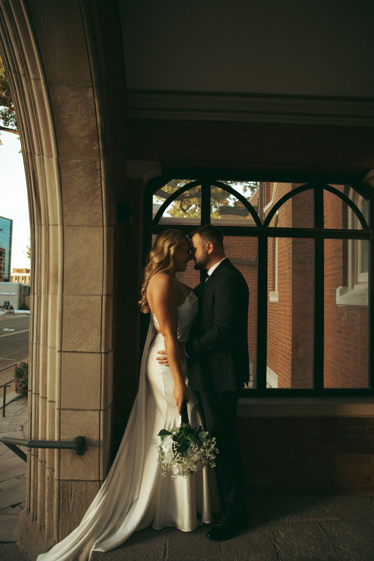 A romantic wedding couple shares an intimate moment under an arched walkway at sunset.