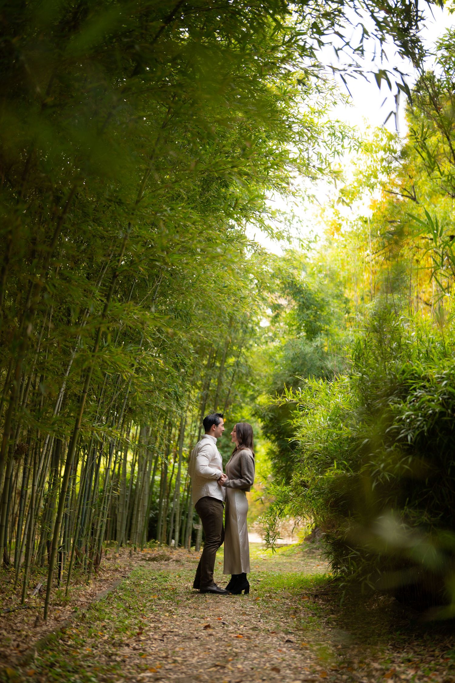 Couple holding each other tenderly on a serene bamboo forest path surrounded by lush greenery.