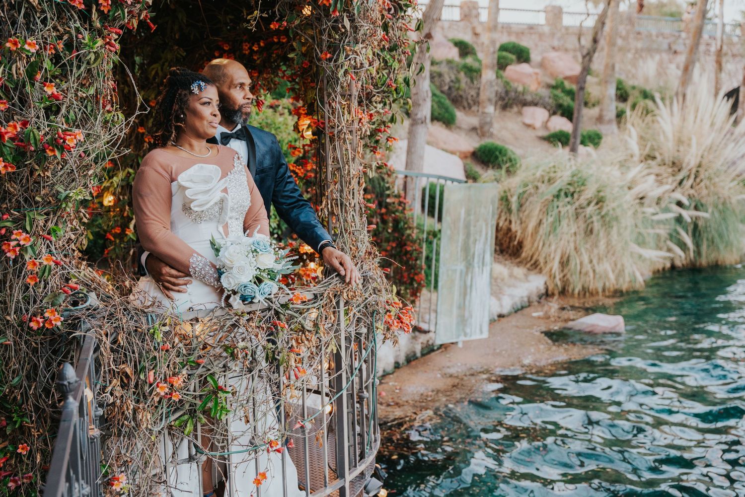A romantic wedding couple embraces on a rustic bridge surrounded by autumn foliage near tranquil water.