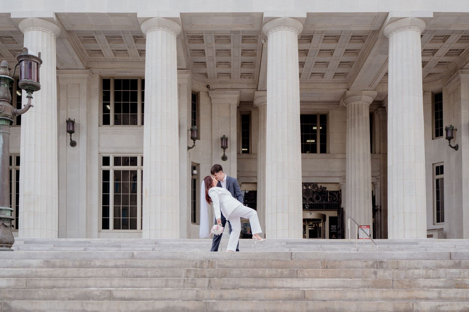 A white columned building exterior with classical architecture features people walking near its entrance.