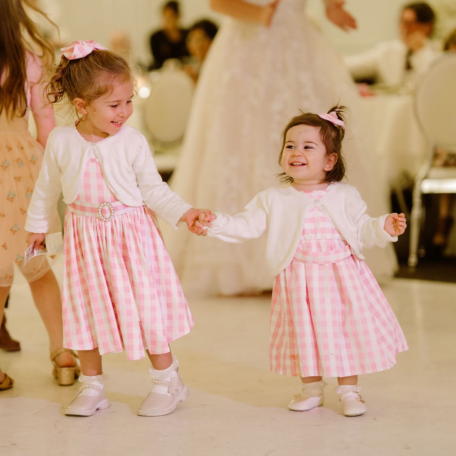 A toddler wearing a pink gingham dress and white shoes walks and dances in various poses.
