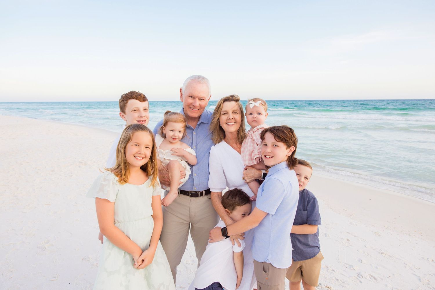 A family wearing white outfits shares a playful moment together on a sandy beach.